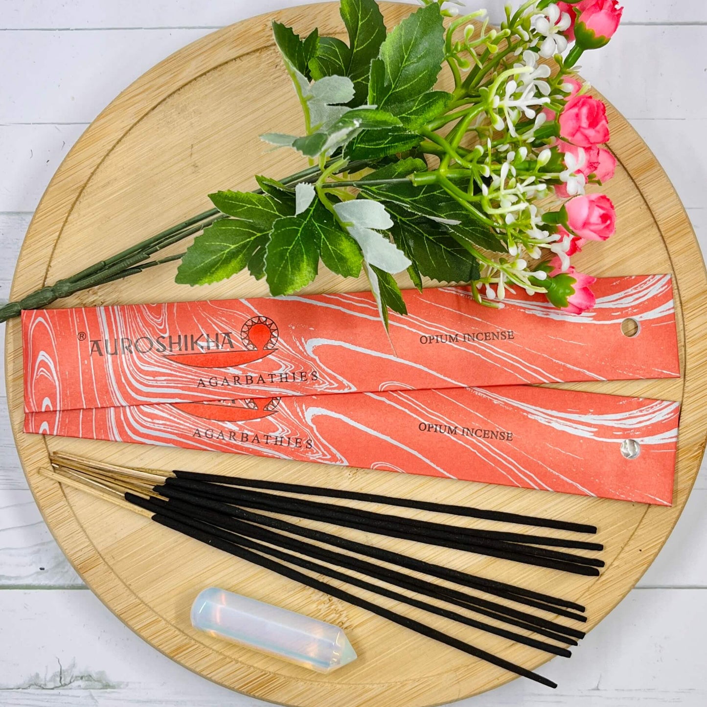 Auroshikha Opium incense pack with incense sticks displayed on a wooden surface, adorned with flowers and leaves.