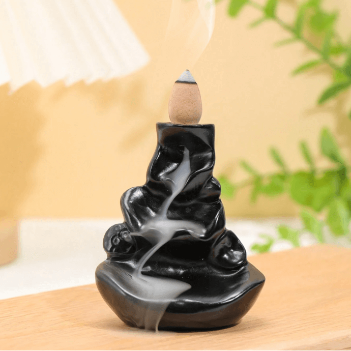 Black wavy incense burner with a wooden incense stick on a neutral background