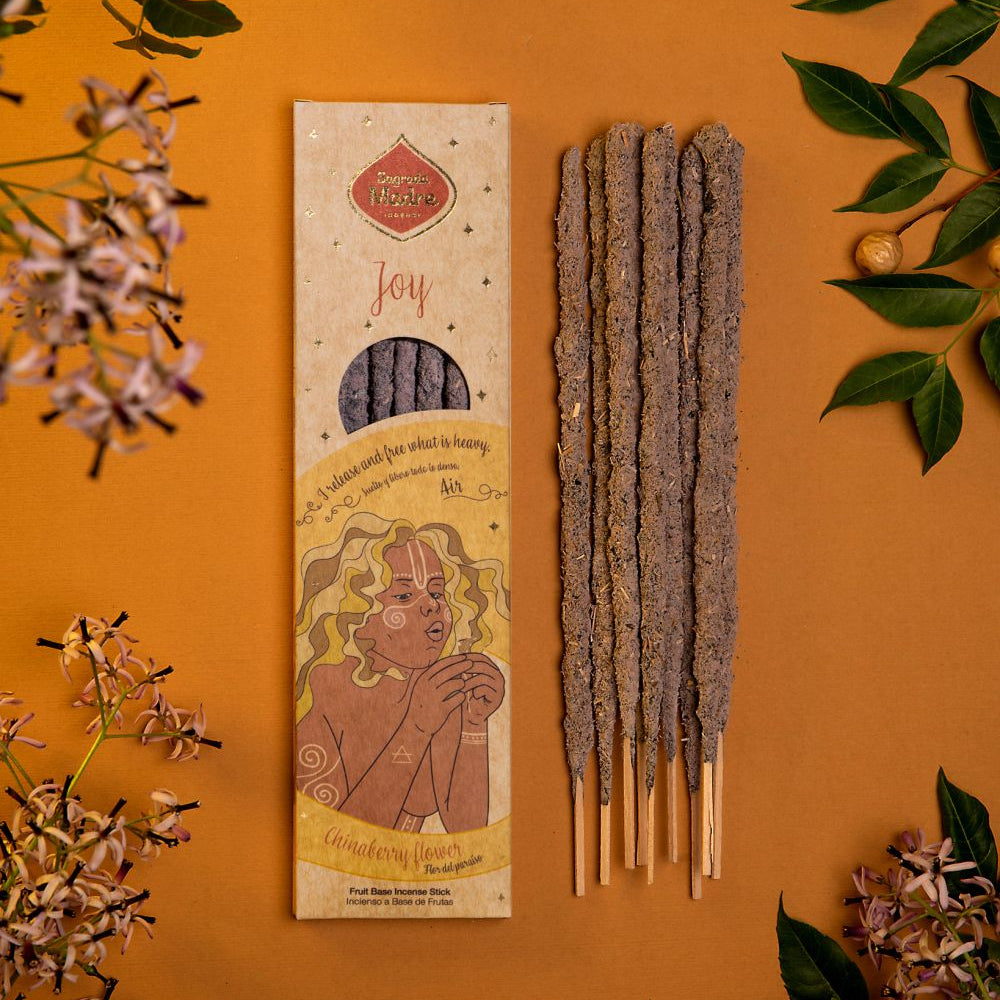 A pack of incense sticks displayed alongside decorative flowers and leaves on an orange background. The packaging features a illustration and text related to the product.