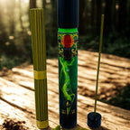 Two incense sticks in decorative holders on a wooden surface with a forest background