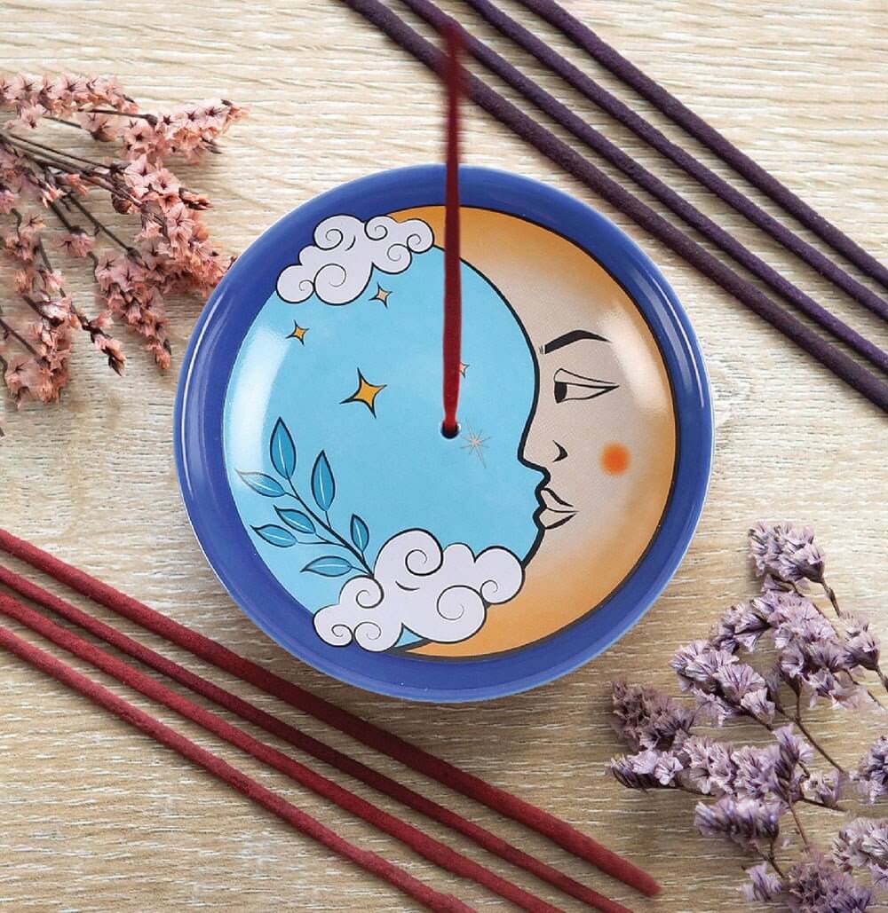 Decorative plate with moon and star design on a wooden surface with incense sticks and flowers.