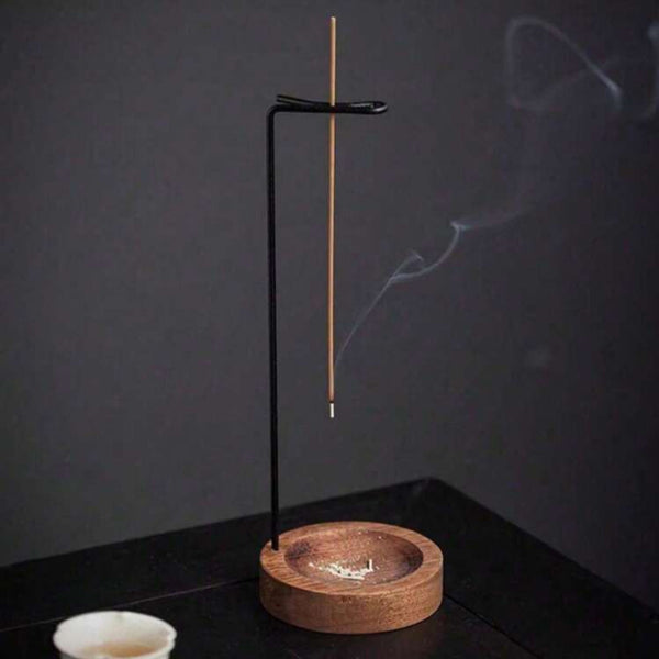 Incense burner with a single incense stick on a dark surface with a cup and saucer in the background.
