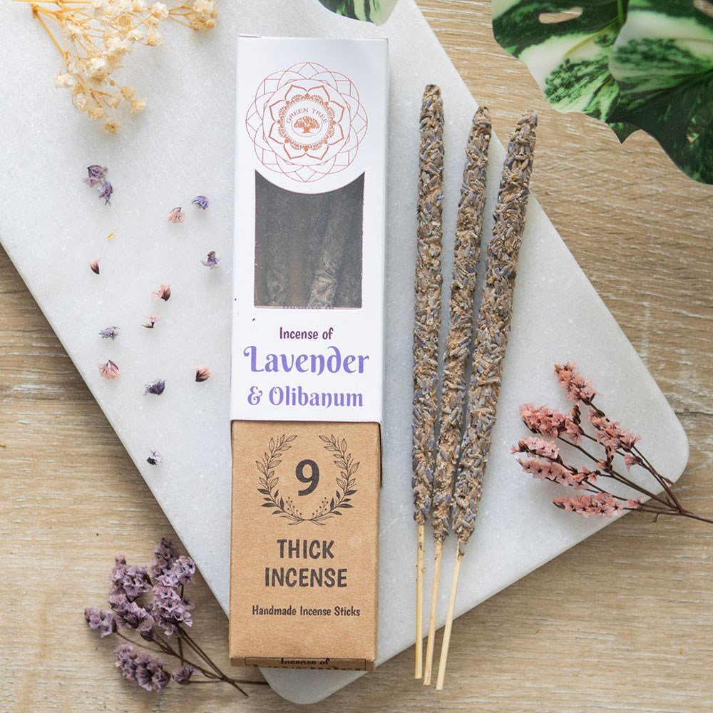 A package of Green Tree brand incense sticks labeled 'Lavender & Olibanum', with nine sticks visible in the packaging, placed on a wooden surface with decorative flowers and a crystal flower in the background.