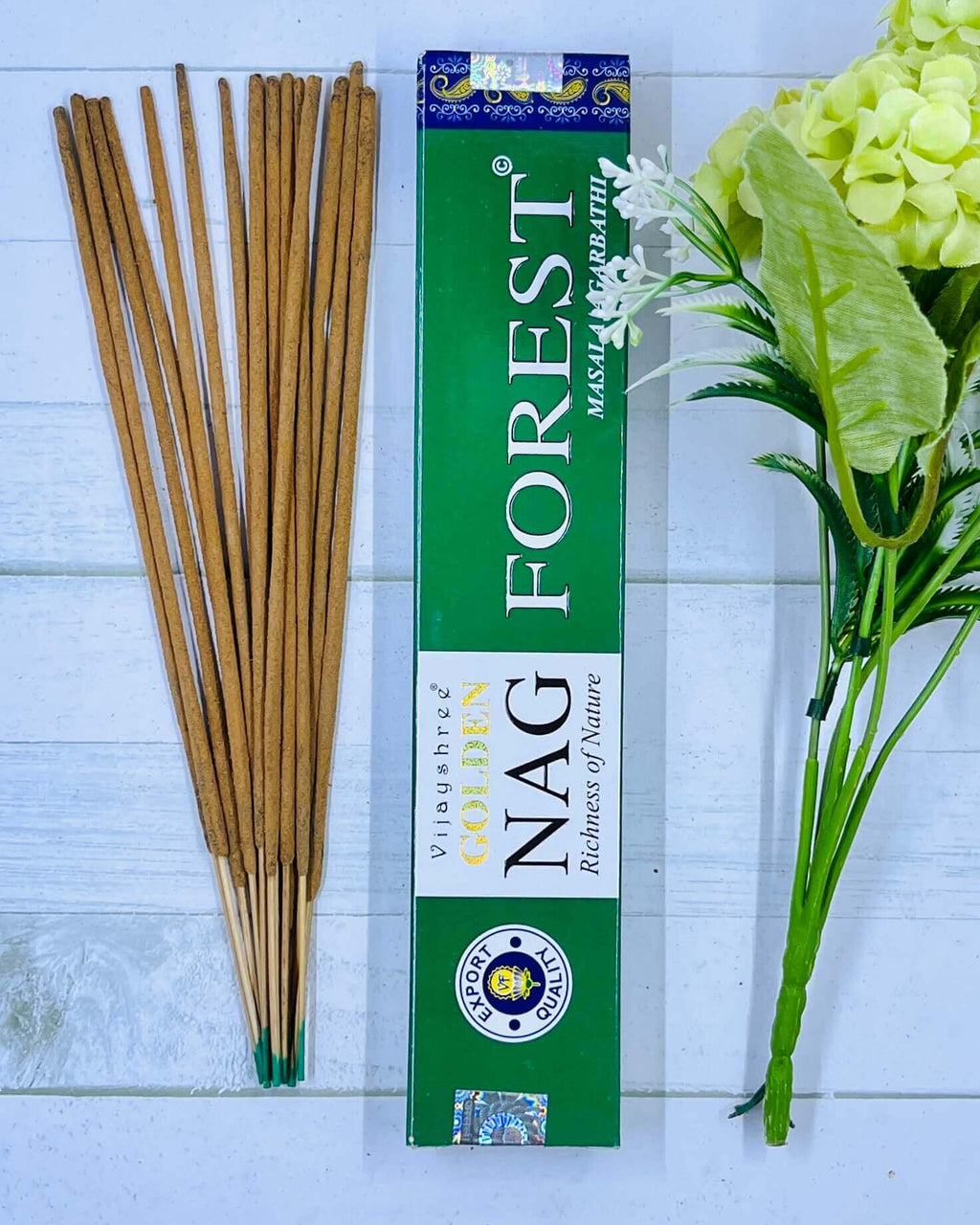 A pack of Vijayshree Golden Nag Forest incense sticks displayed alongside a green floral arrangement, with the product's packaging visible in the background.