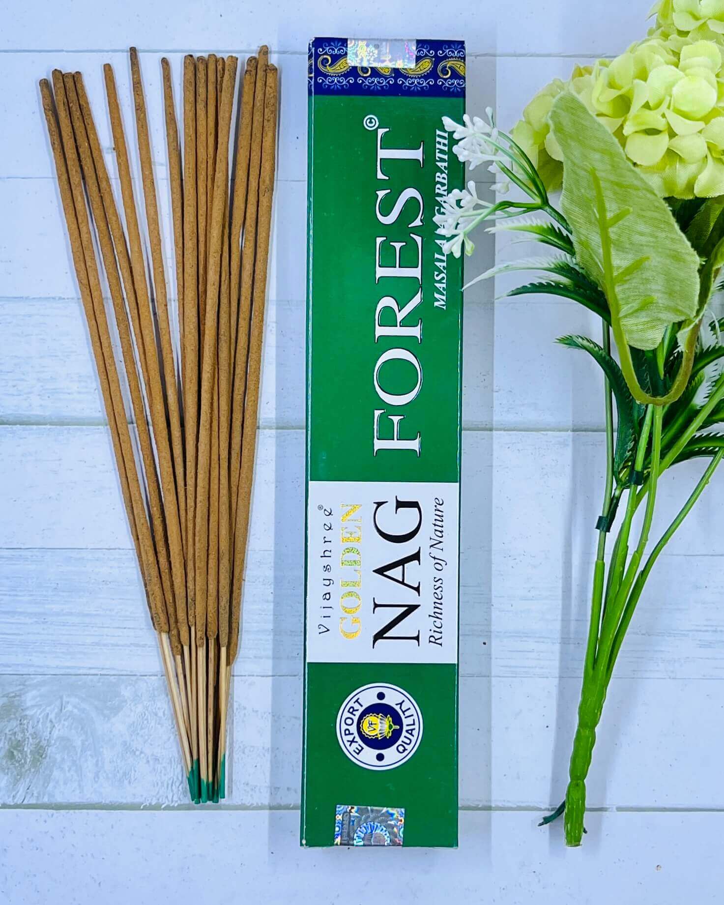 A pack of Vijayshree Golden Nag Forest incense sticks displayed alongside a green floral arrangement, with the product's packaging visible in the background.