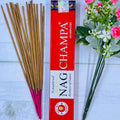 A pack of Vijayshree Golden Nag Champa incense sticks displayed alongside a bouquet of pink flowers.