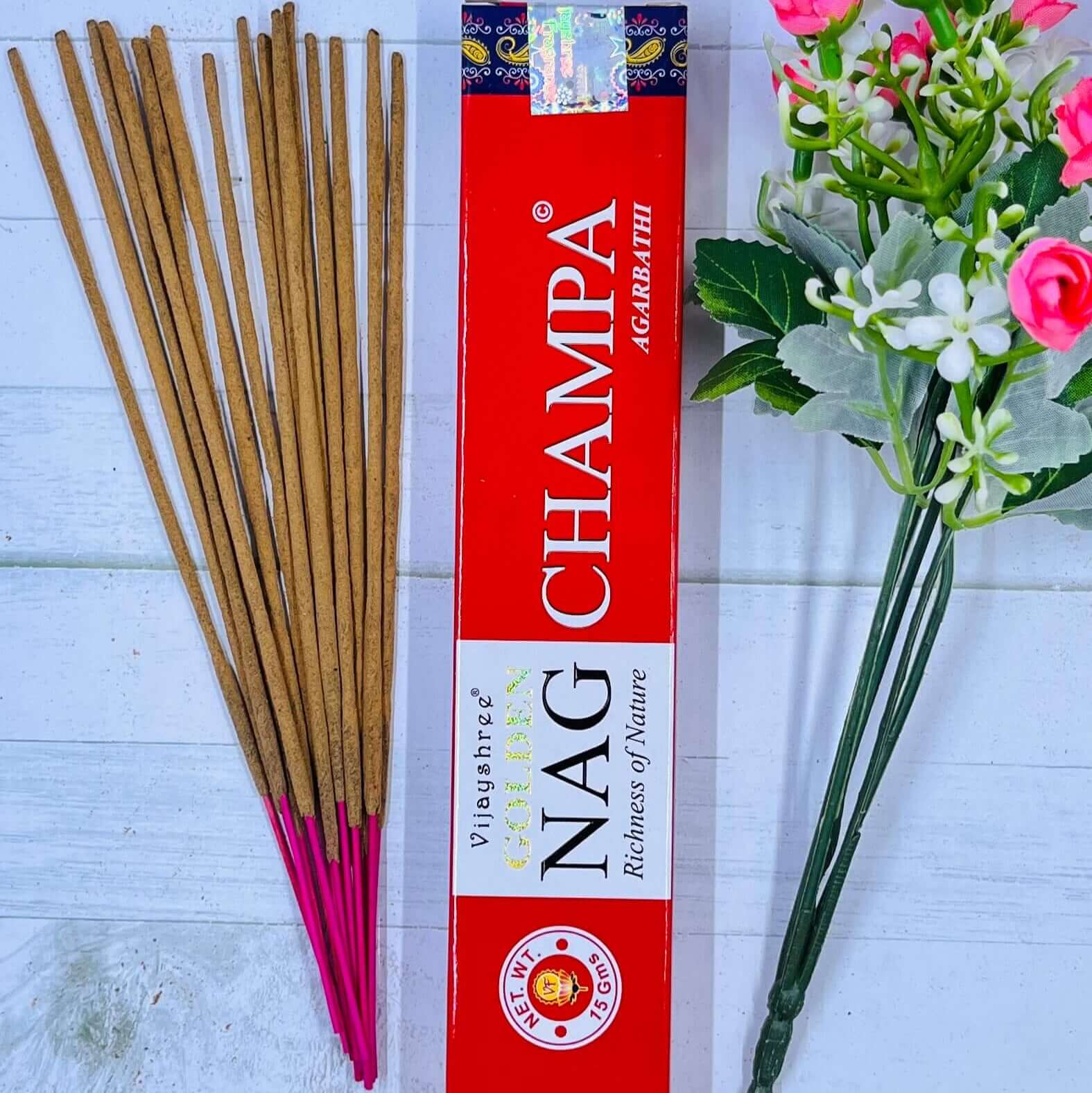 A pack of Vijayshree Golden Nag Champa incense sticks displayed alongside a bouquet of pink flowers.