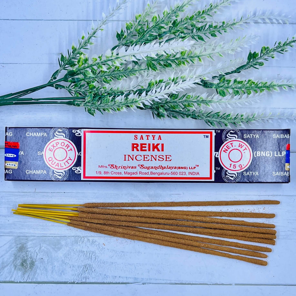 A packet of Satya REIKI incense sticks displayed alongside a sprig of dried herbs, placed on a wooden surface.