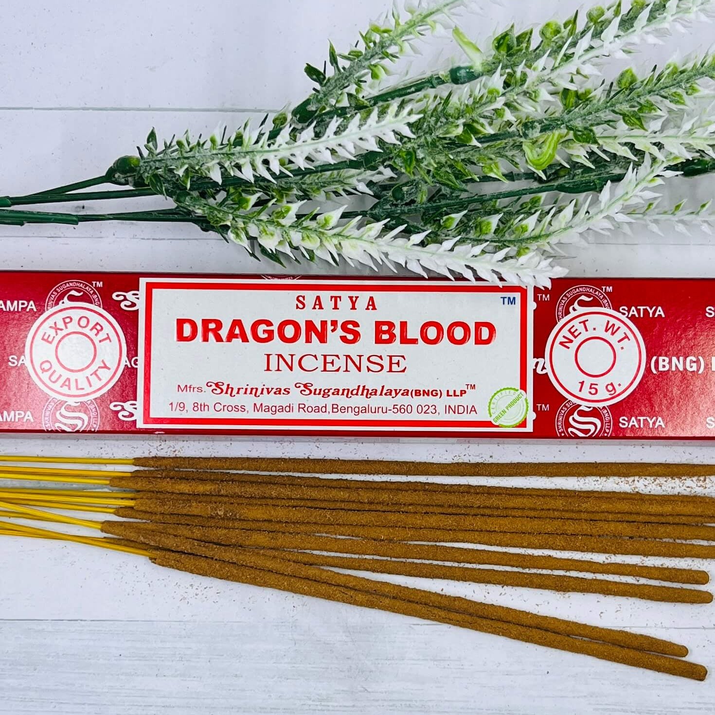 A packet of Satya Dragon's Blood incense sticks displayed alongside a sprig of dried herbs on a wooden surface.
