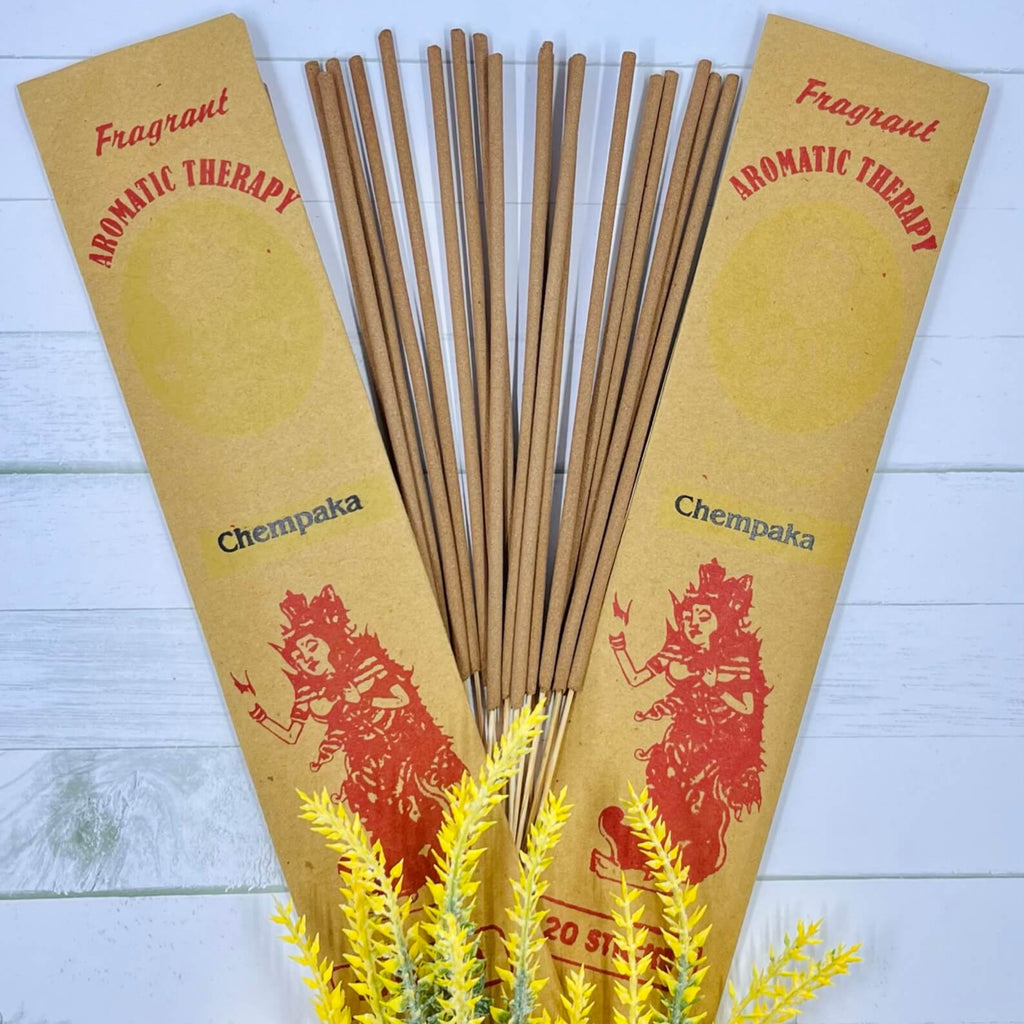 A packet of Balinese Chempaka incense sticks displayed alongside decorative yellow flowers, with the incense packet showing traditional Balinese artwork.