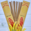 A packet of Balinese Chempaka incense sticks displayed alongside decorative yellow flowers, with the incense packet showing traditional Balinese artwork.