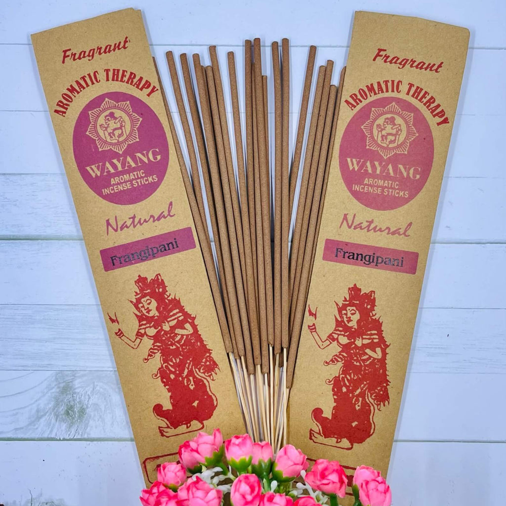 A packet of Balinese Frangipani incense sticks displayed alongside a bouquet of pink roses, with packaging featuring traditional Balinese artwork.