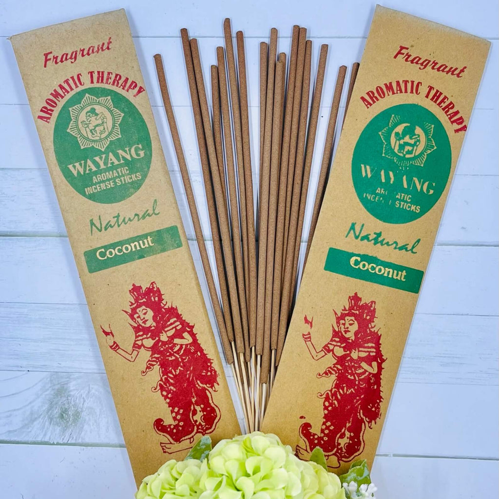A packet of Balinese Coconut Incense with 20 sticks, displayed alongside a decorative flower arrangement. The packaging features a red traditional Bali figure illustration with 'Natural Coconut' written below.