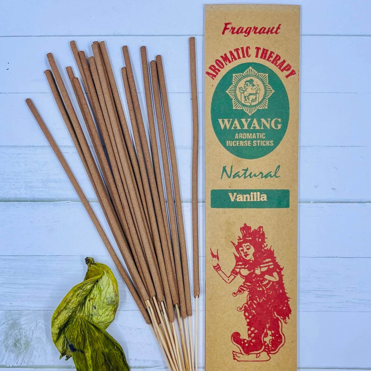 A packet of Balinese vanilla incense sticks displayed alongside some green leaves on a wooden surface.