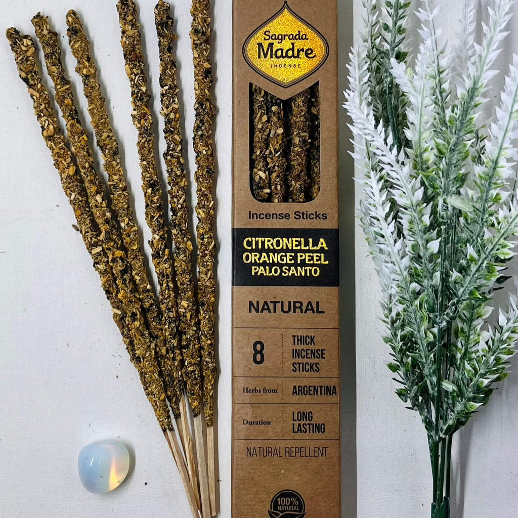 A box of Sagrada Madre natural incense sticks with citronella and orange, alongside decorative plants and a lit candle.