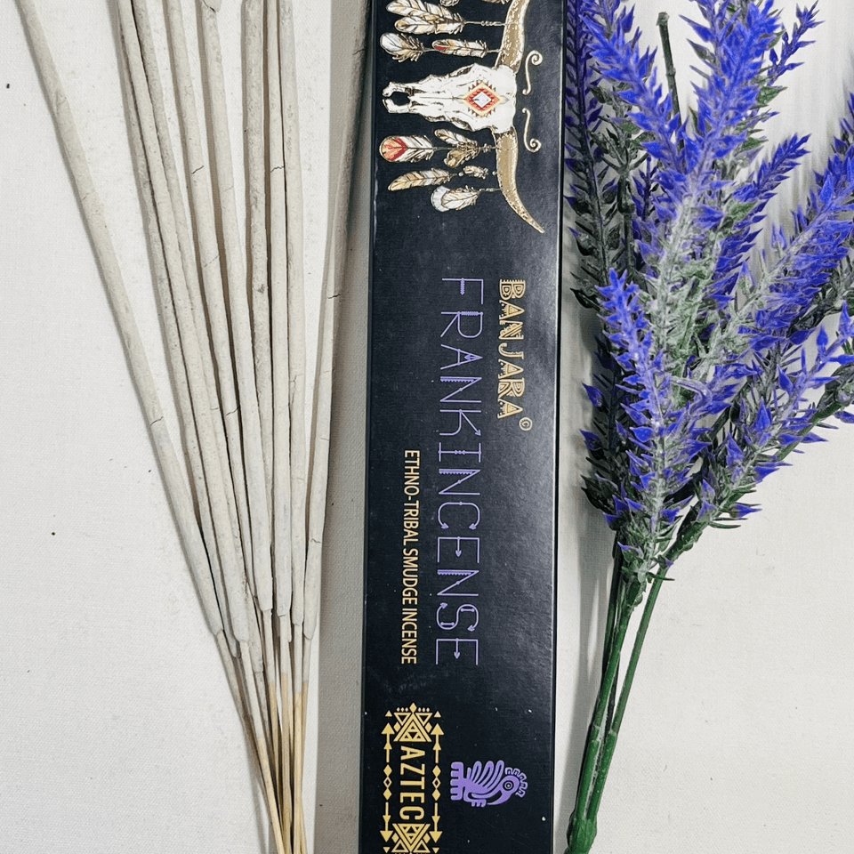 A packet of Banjara Aztec incense sticks with Frankincense fragrance, displayed alongside decorative purple flowers.