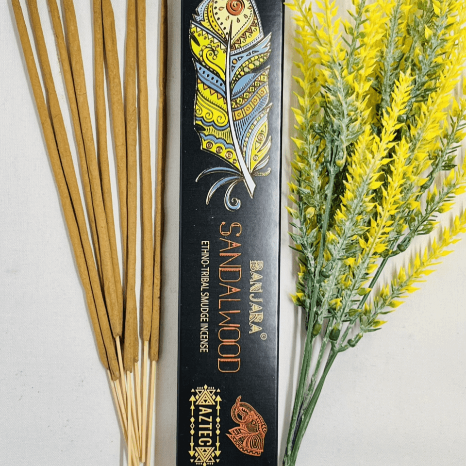 A packet of Banjara Aztec Sandalwood incense sticks displayed alongside some decorative yellow flowers.