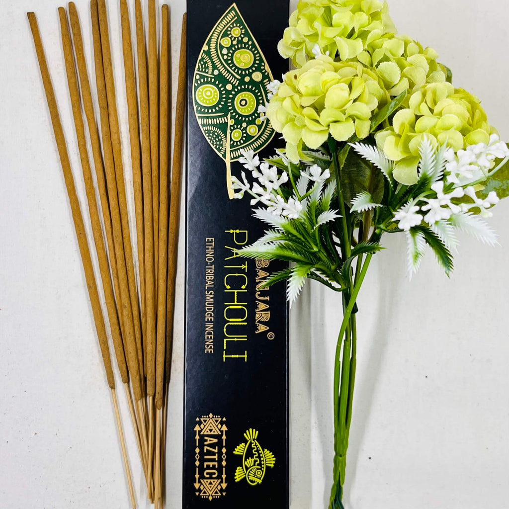 A packet of Banjara Aztec incense sticks with a green and yellow floral design next to a bouquet of green and white flowers.