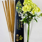 A packet of Banjara Aztec incense sticks with a green and yellow floral design next to a bouquet of green and white flowers.