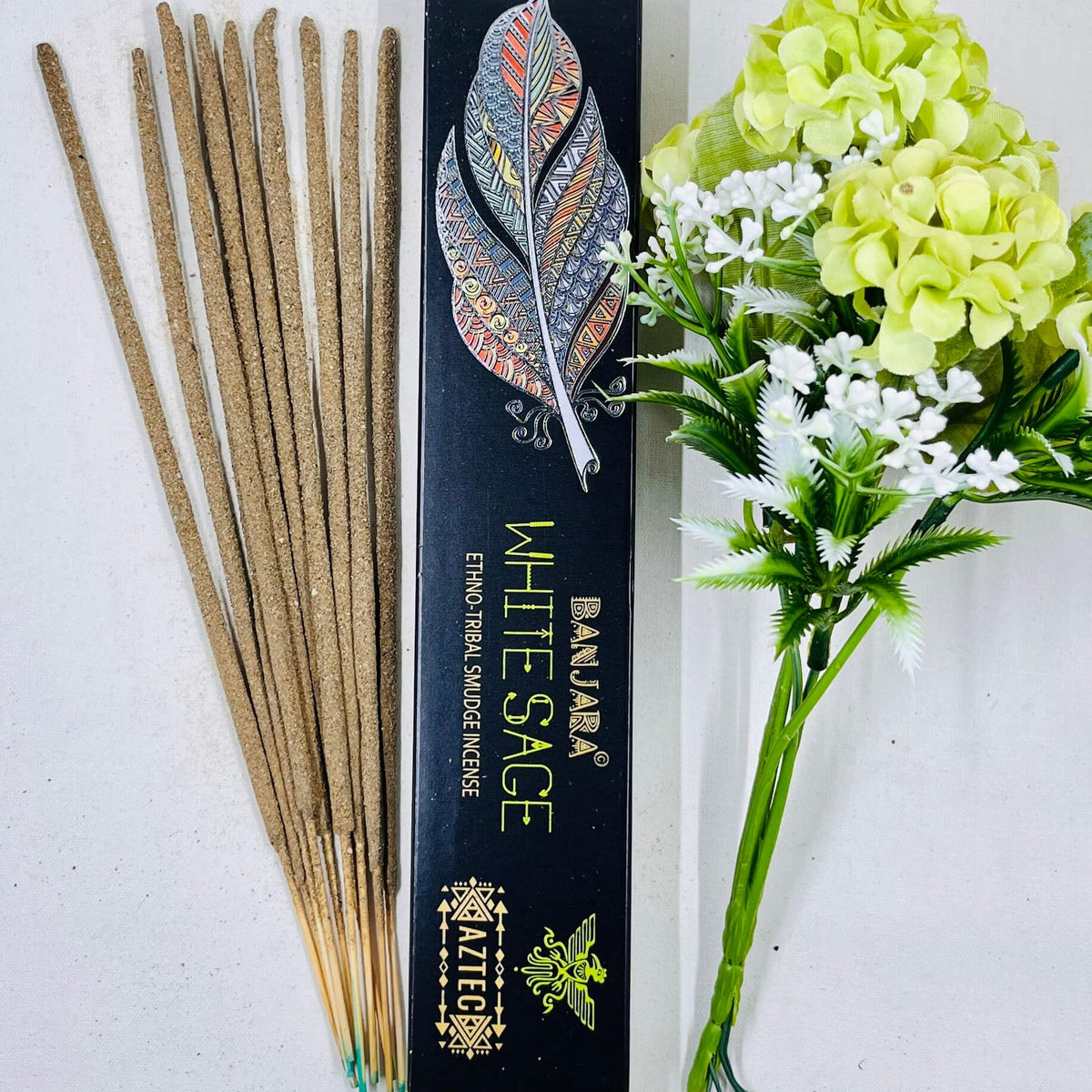 A packet of Banjara Aztec incense sticks labeled 'WHITE SAGE' displayed alongside a bundle of fresh flowers.