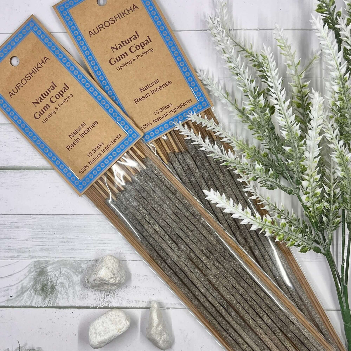 A pack of Auroshikha Natural Gum Copal Incense with 10 long dhoop sticks, displayed alongside decorative stones and herbs on a white wooden surface.