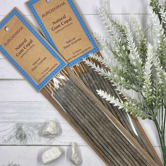 A pack of Auroshikha Natural Gum Copal Incense with 10 long dhoop sticks, displayed alongside decorative stones and herbs on a white wooden surface.