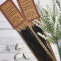 Incense sticks packaged in a cardboard holder with a label that reads 'Auroshikha Sacred Myrrh & Frankincense'. The sticks are displayed in front of a white wooden background with some foliage at the bottom.
