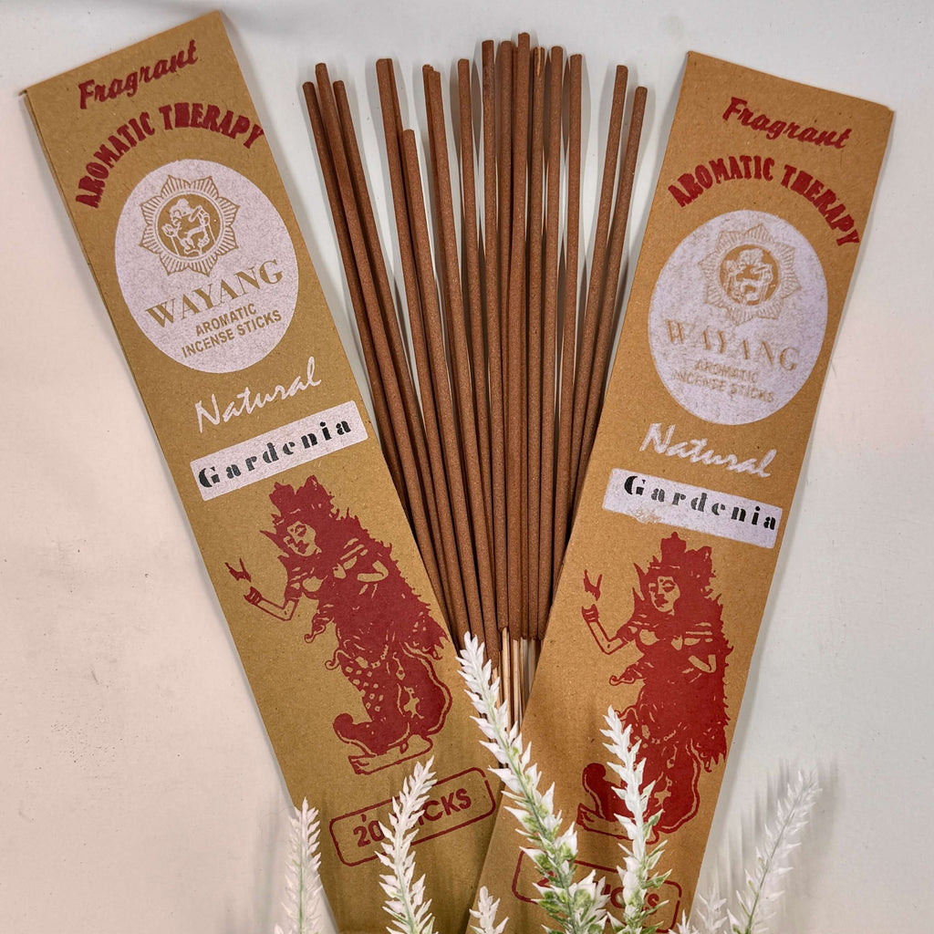 A packet of Wayang brand incense with 'GARDENIA' written on it, alongside a bundle of brown incense sticks. The packets and sticks are displayed against a white background with some green foliage.