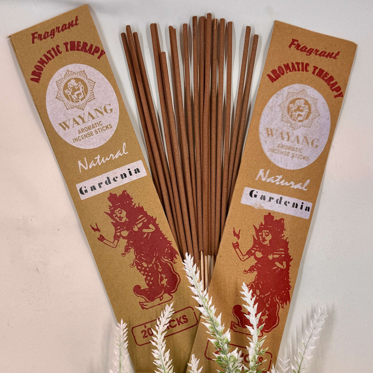 A packet of Wayang brand incense with 'GARDENIA' written on it, alongside a bundle of brown incense sticks. The packets and sticks are displayed against a white background with some green foliage.