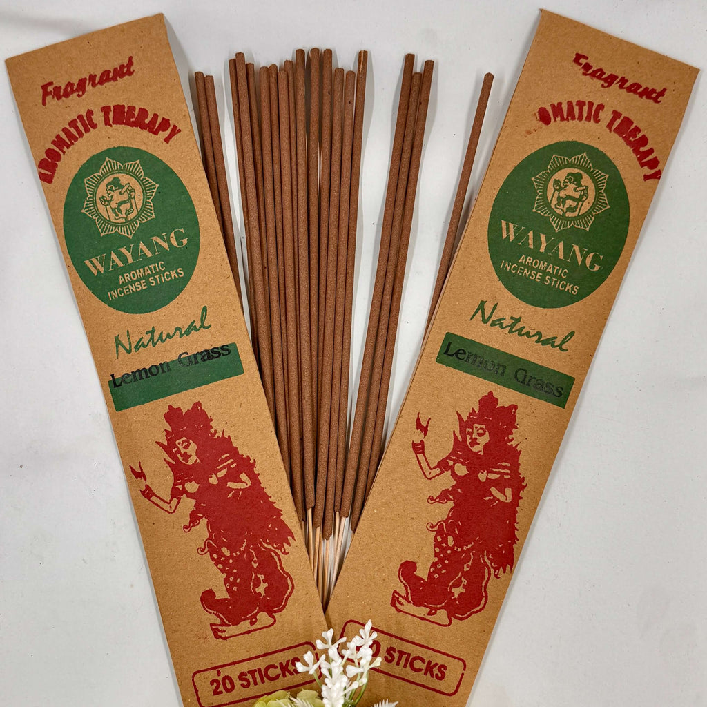 A bundle of brown incense sticks labeled 'Wayang', with packaging that includes the text 'Natural' and an illustration of a mouse. There are 20 sticks per packet, displayed with a decorative flower arrangement in the foreground.