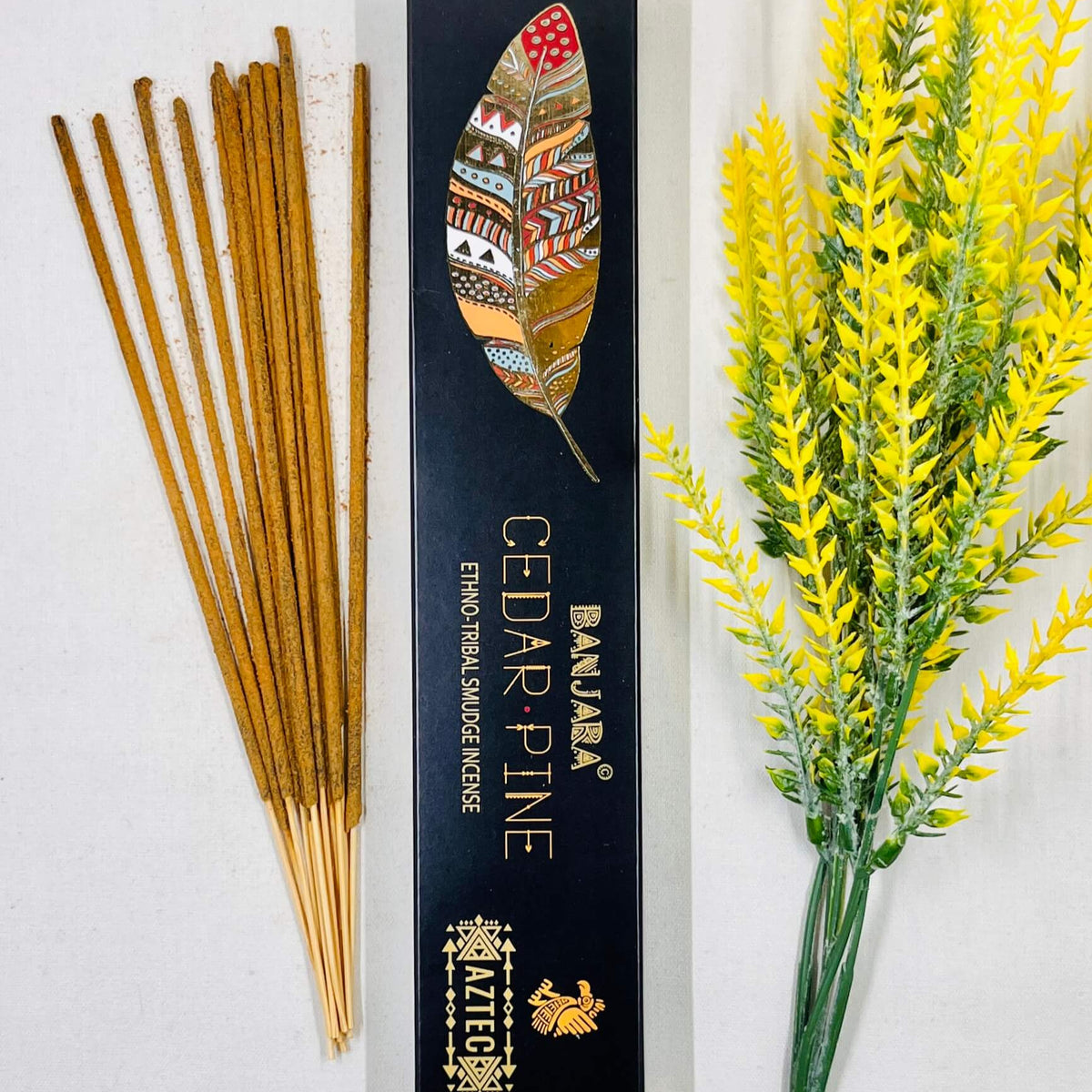 A packet of Banjara Aztec incense sticks with Cedar Pine fragrance, displayed alongside decorative yellow flowers.