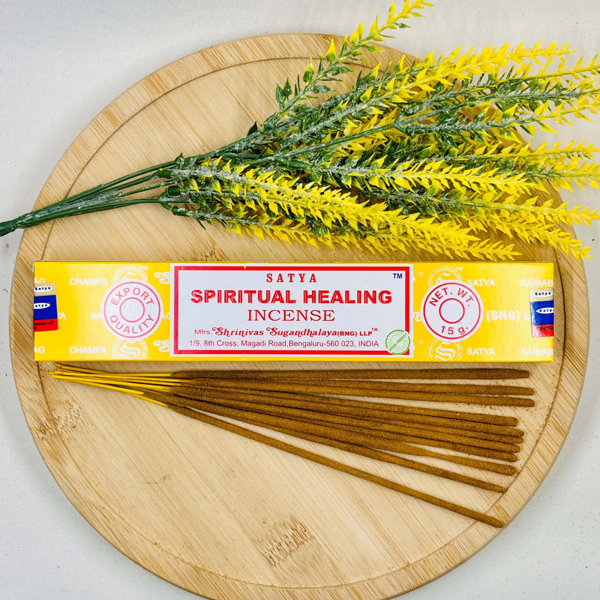 A packet of Satya Spiritual Healing incense sticks displayed alongside yellow flowers on a wooden board.