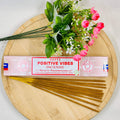 A packet of Satya Positive Vibes incense placed on a wooden surface with a bouquet of pink flowers beside it.