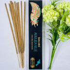 A packet of Banjara Aztec incense sticks with the Arruda Rue fragrance, displayed alongside green artificial flowers. The packaging features a colorful traditional design.