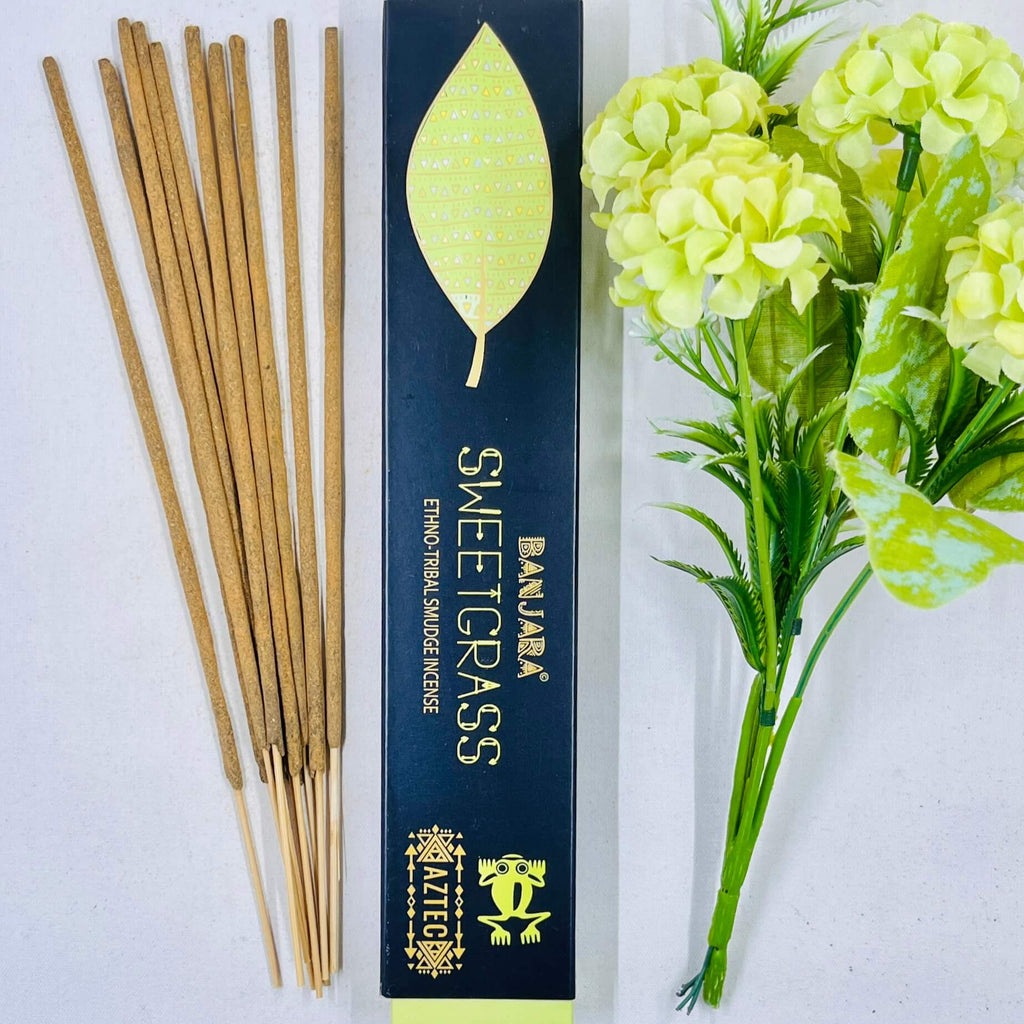 A packet of Banjara Aztec Sweet Grass incense sticks displayed alongside green artificial flowers.