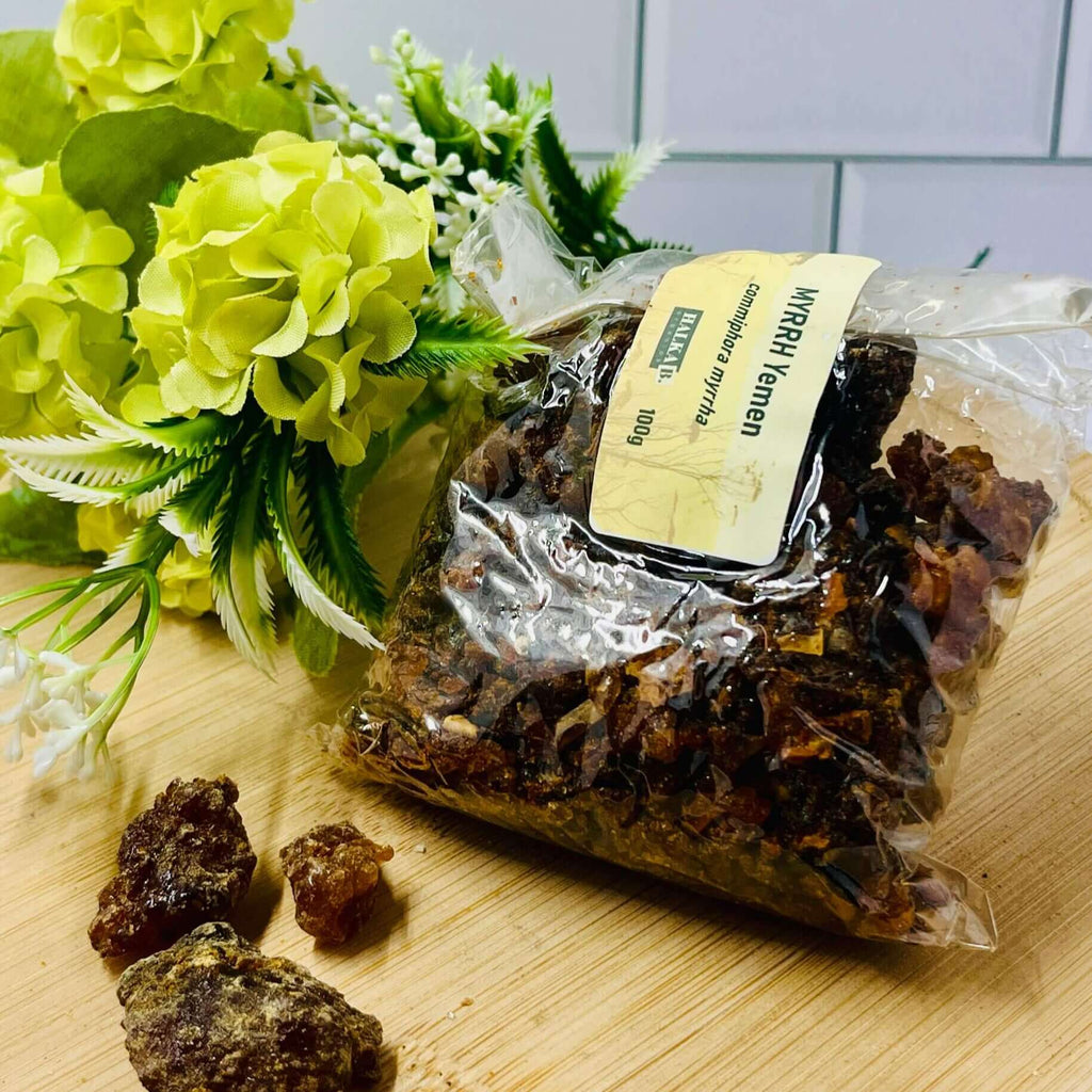 A clear plastic bag containing brown resin pieces with a label, placed on a wooden surface with yellow flowers in the background.