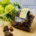A clear plastic bag containing brown resin pieces with a label, placed on a wooden surface with yellow flowers in the background.