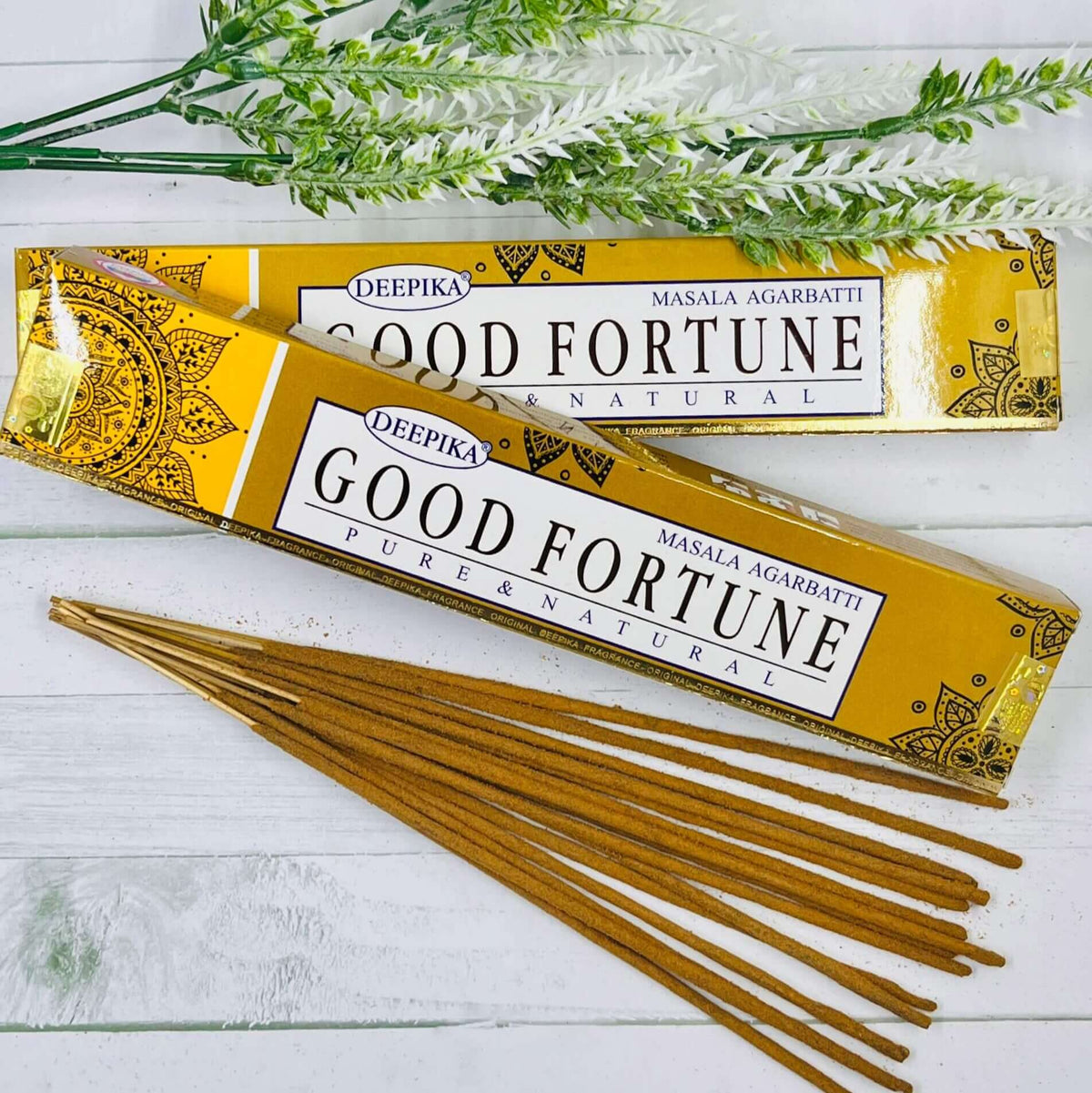 A pack of Deepika Good Fortune incense sticks displayed alongside decorative greenery against a white wooden background.