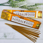 A pack of Deepika Sandalwood incense sticks displayed alongside greenery against a white wooden background.