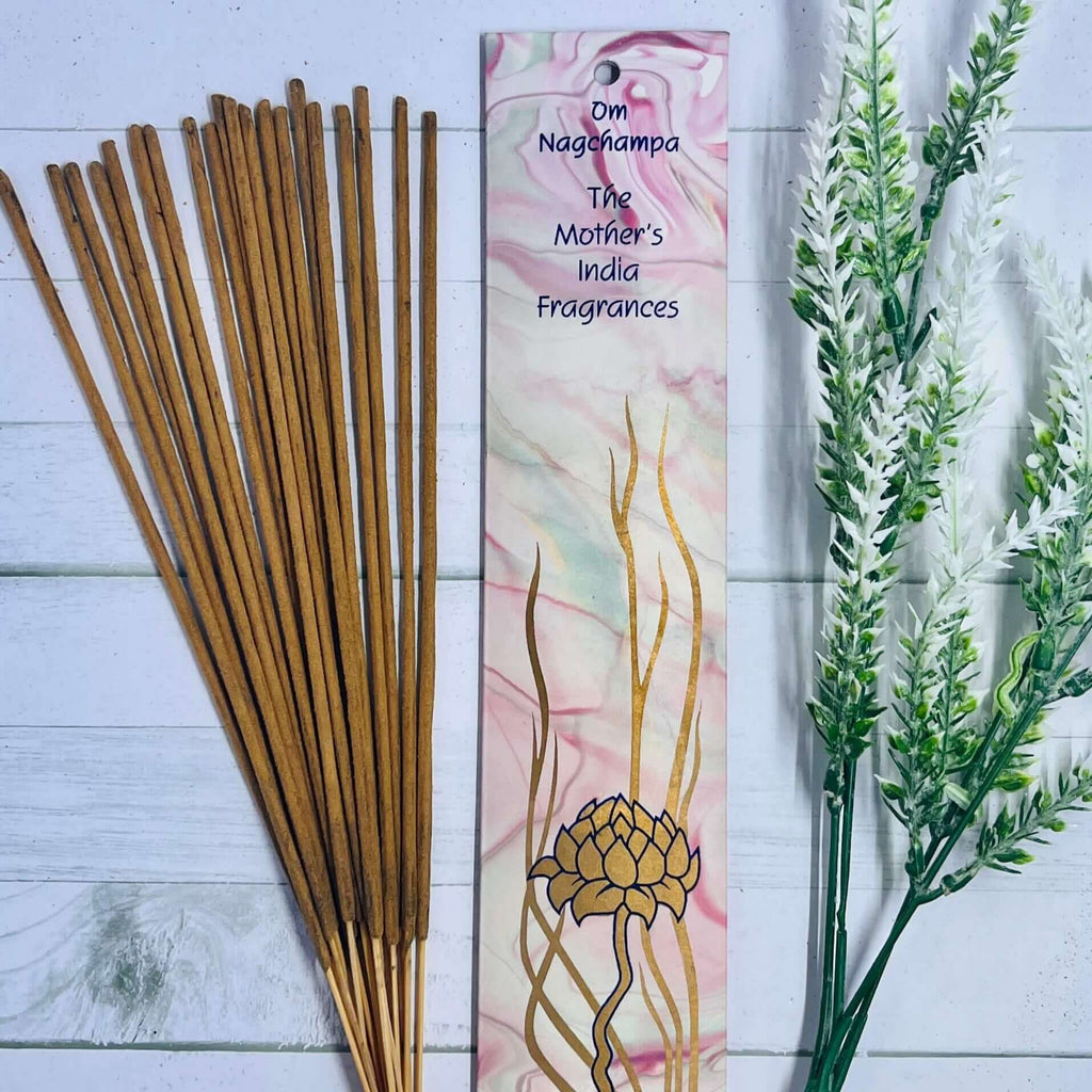 A pack of Mother's India Om Nag Champa incense sticks displayed alongside decorative floral elements on a wooden surface.