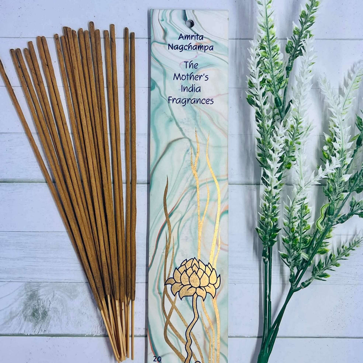A pack of Mother's India Amrita Nag Champa incense sticks displayed alongside decorative foliage on a wooden surface.