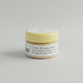 A small round tin of sandal powder sits on a wooden desk with a black keyboard in the background. The lid is pale yellow with a white label reading 'SANDAL POWDER', '30 g', and '100% PURE'.