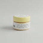 A small round tin of sandal powder sits on a wooden desk with a black keyboard in the background. The lid is pale yellow with a white label reading 'SANDAL POWDER', '30 g', and '100% PURE'.