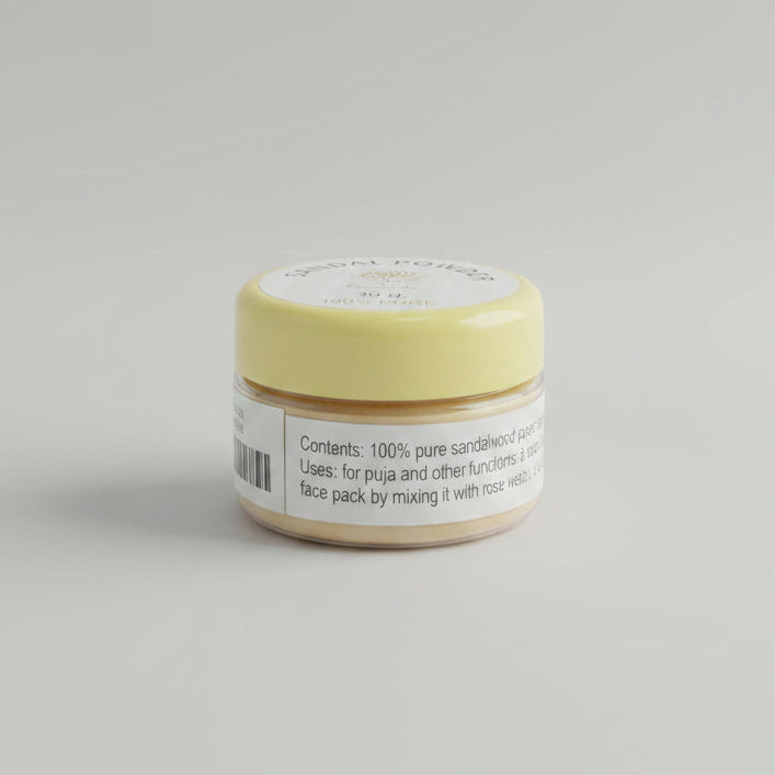A small round tin of sandal powder sits on a wooden desk with a black keyboard in the background. The lid is pale yellow with a white label reading 'SANDAL POWDER', '30 g', and '100% PURE'.