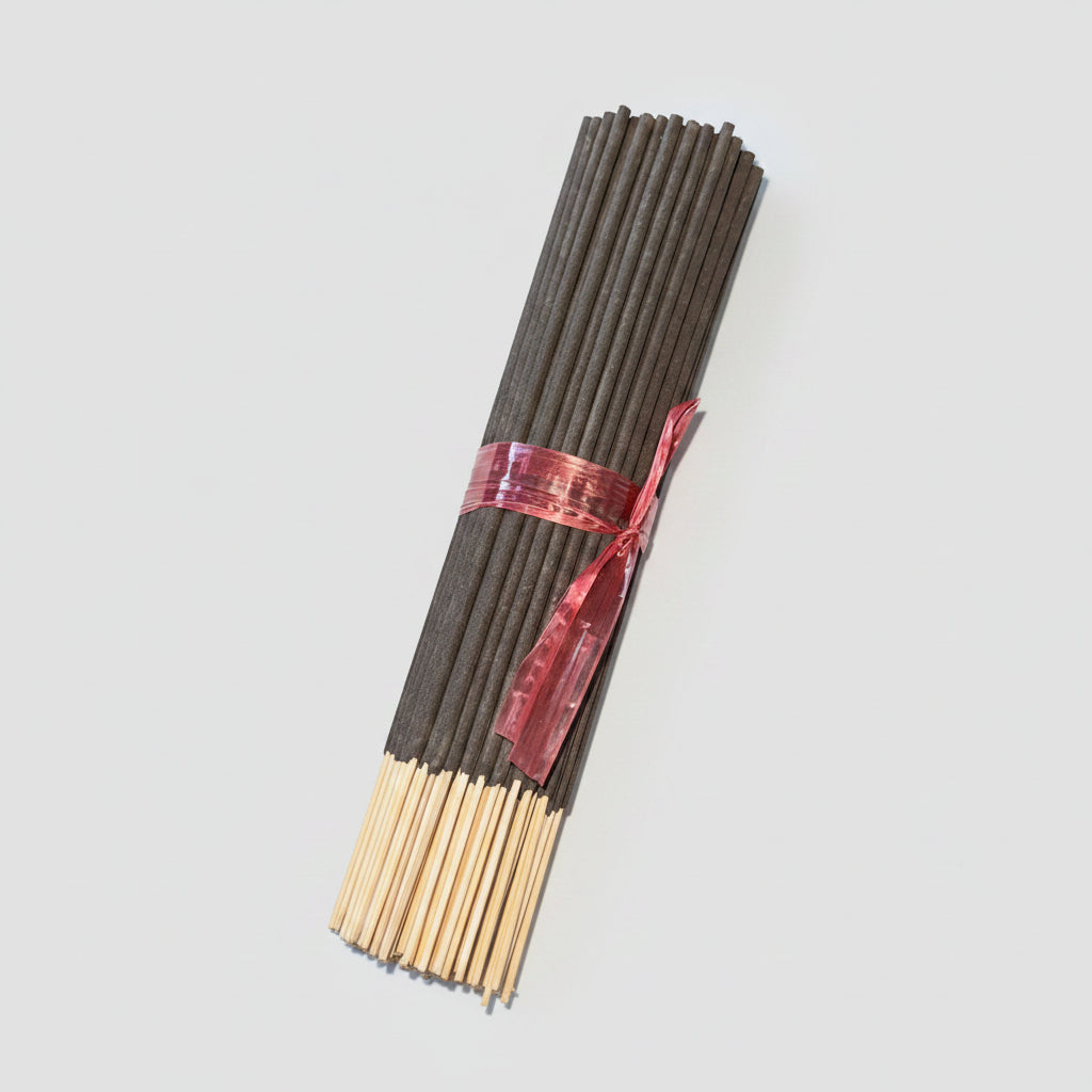 A bundle of incense sticks tied with a red ribbon, placed diagonally on a dark brown wooden floor.