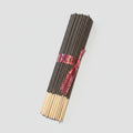 A bundle of incense sticks tied with a red ribbon, placed diagonally on a dark brown wooden floor.