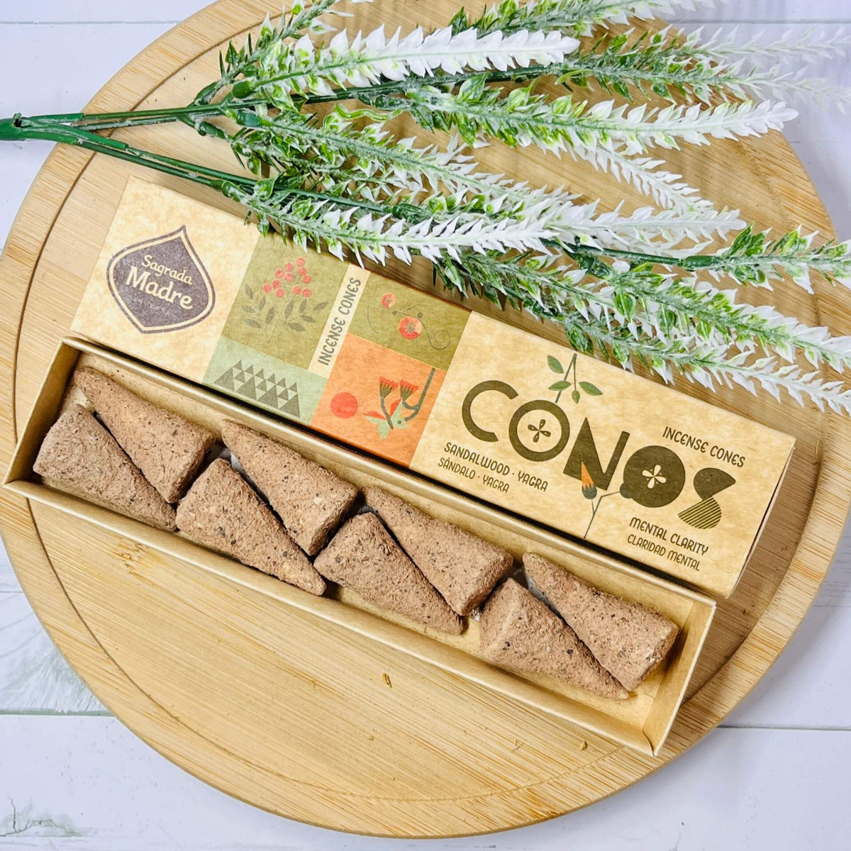 A pack of incense cones from Sagrada Madre displayed in a natural brown box, with decorative dry leaves on top, against a wooden background.