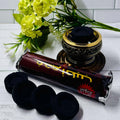 Charcoal discs and incense rolls placed on a white surface with a decorative holder and yellow flowers in the background.