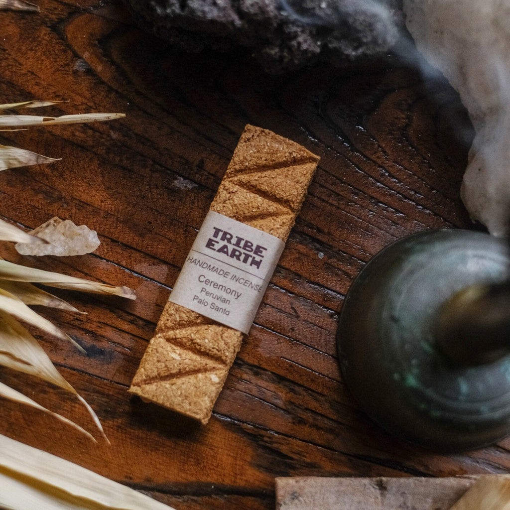 A single plank of incense labeled 'Tribe Earth' is shown alongside burning incense and natural elements like leaves on a wooden surface.