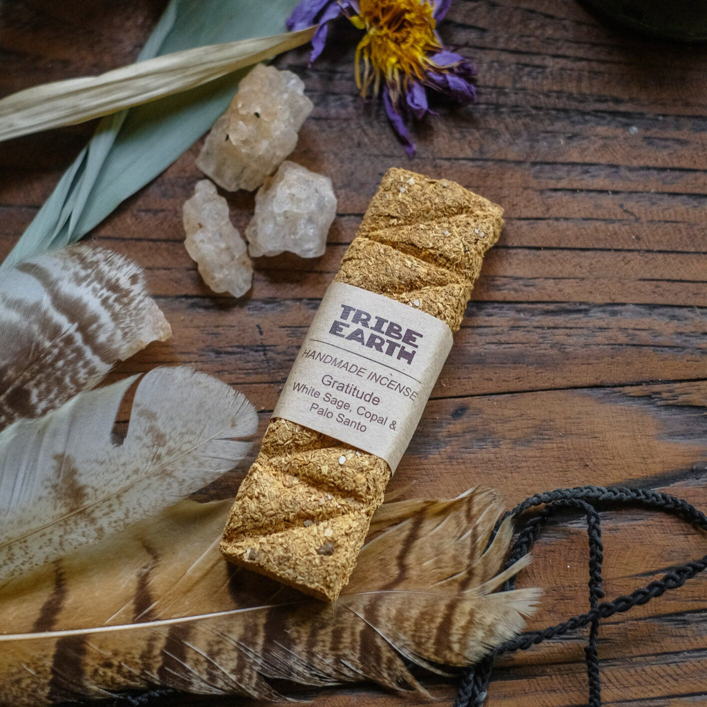 Handmade incense plank surrounded by natural elements such as leaves, flowers, and crystals on a wooden surface.